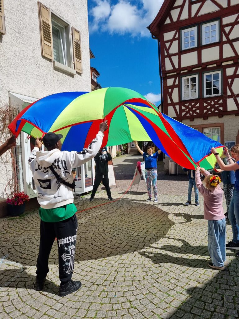 Kinder, Jugendliche und Erwachsene spielen mit einem bunten Schwungtuch